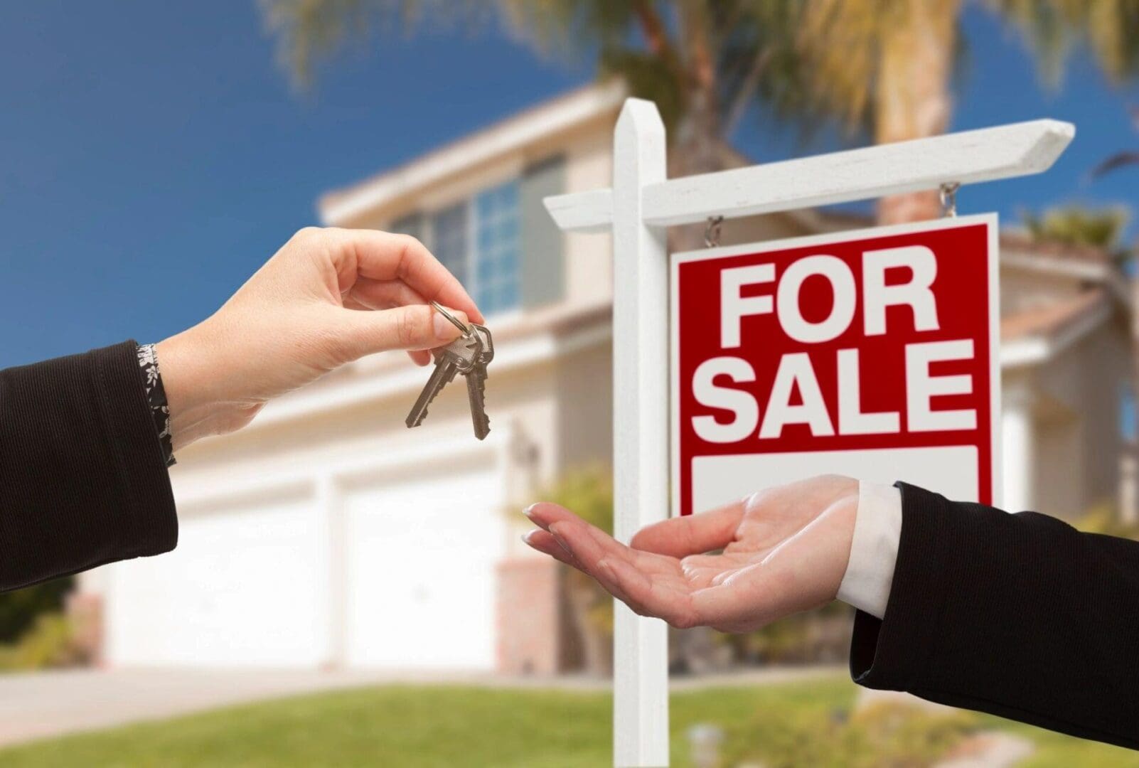 A person handing keys to another person in front of a house.