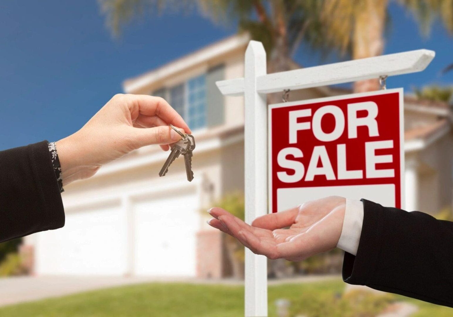 A person handing keys to another person in front of a house.